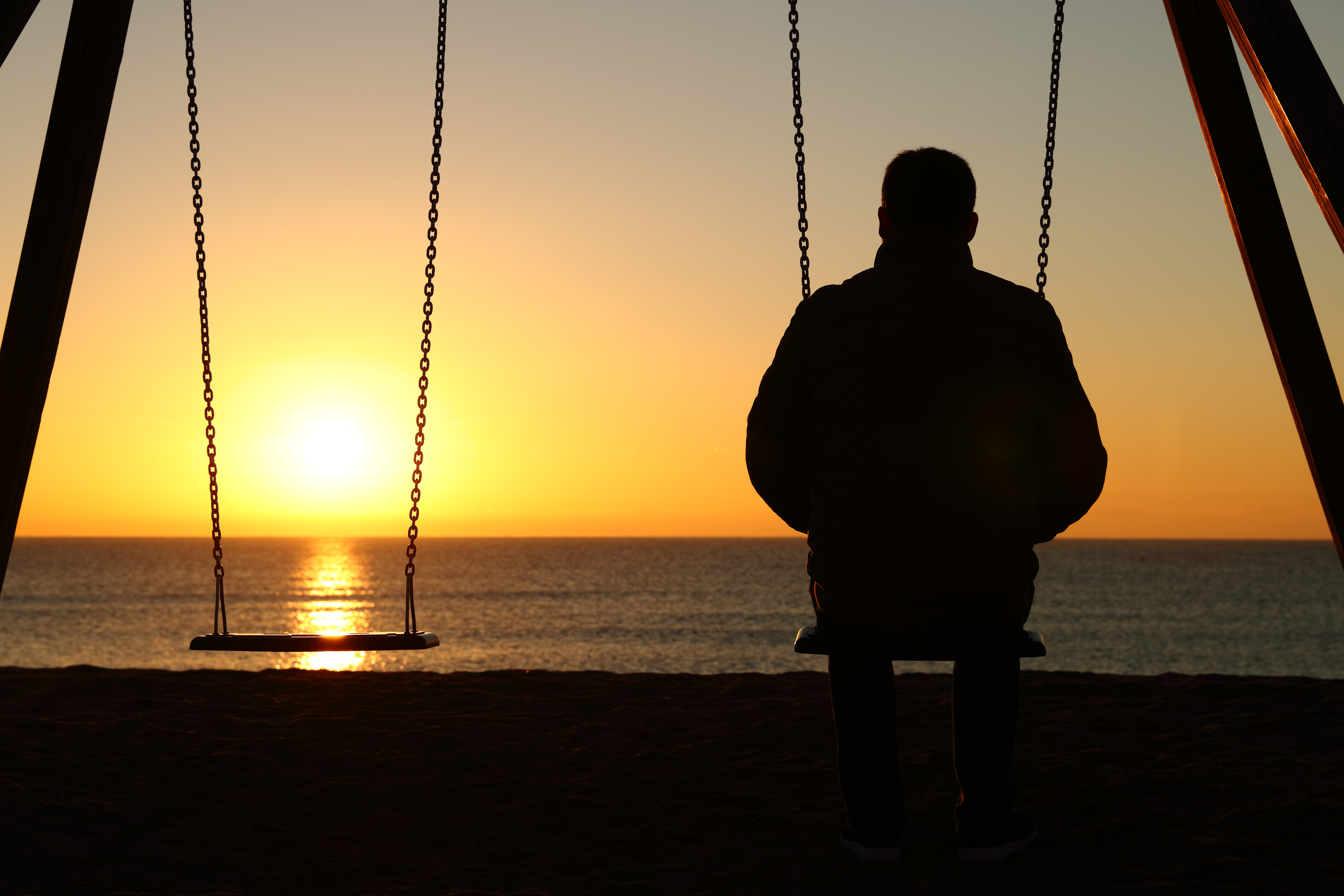 Mand sidder på en gynge og kigger ud over havet på solnedgang