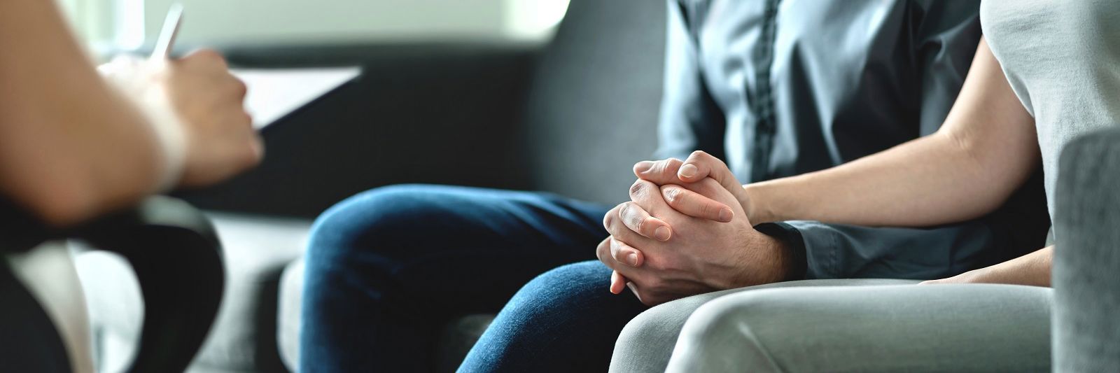 Et par sidder i en sofa og holder i hånden overfor sidder en fagperson