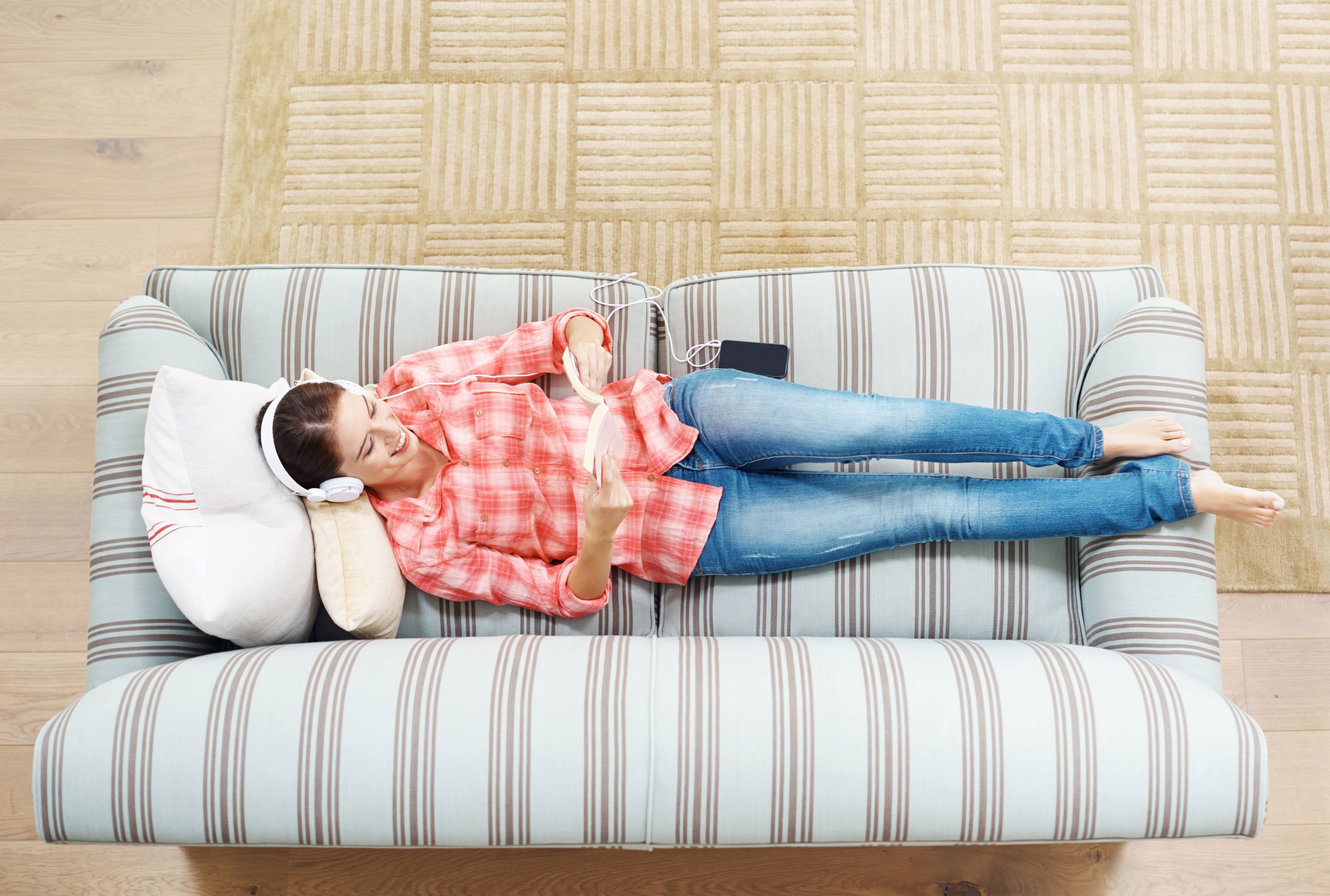 Kvinde ligger i sofa med en bog og en høretelefoner